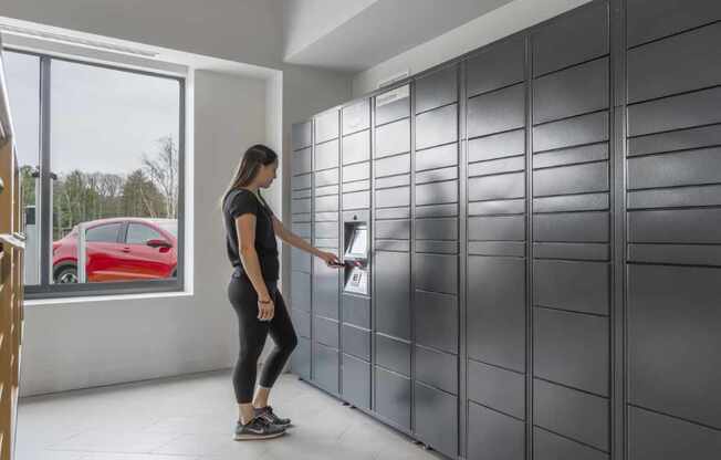 a woman in a black shirt and black leggings opens a drawer in a gray locker