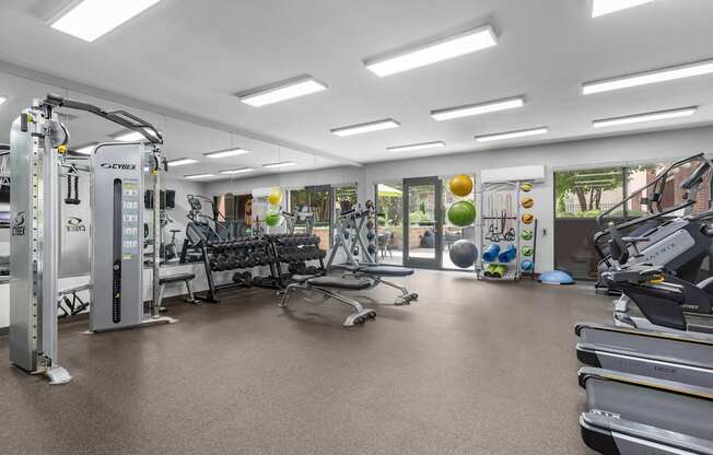 A gym with a variety of equipment including treadmills, weights, and exercise balls.