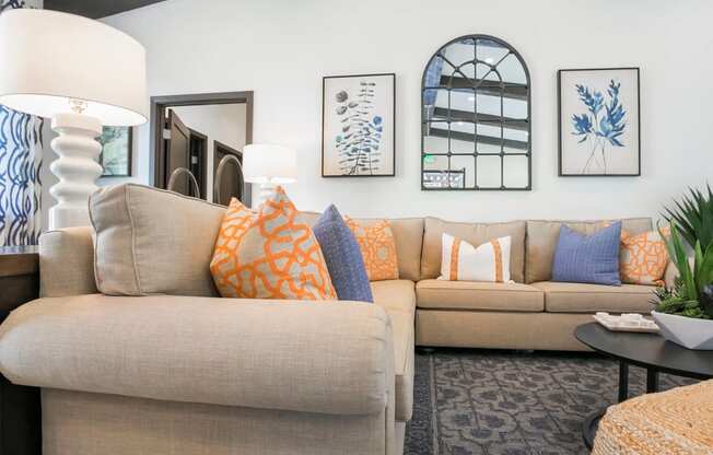 a living room with a tan couch and blue and orange pillows