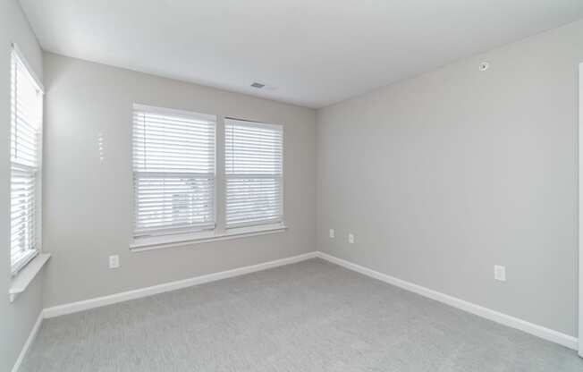 an empty bedroom with two windows and white carpeting