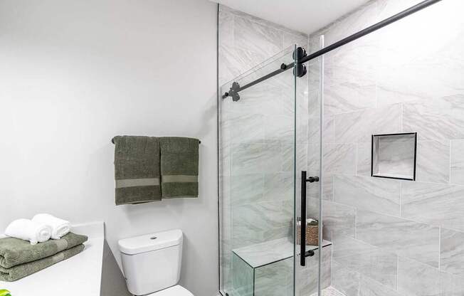 A bathroom with a toilet, a towel, and a glass shower door.