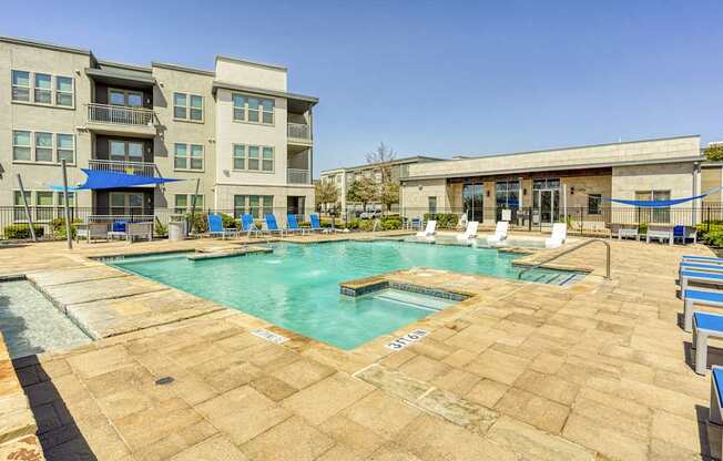 A large outdoor swimming pool with a patio area and a building in the background.