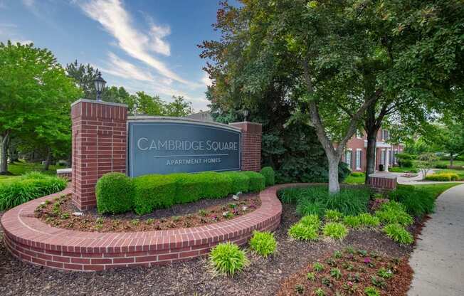 A sign for Cambridge Square Apartment Homes is surrounded by a brick border and greenery.