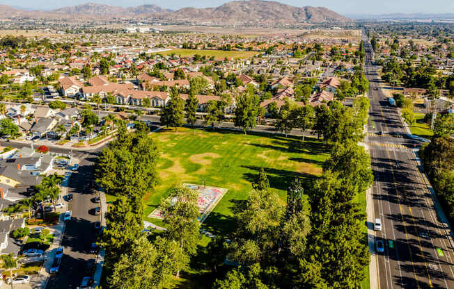 A suburban area with a large green space and a road running through it.
