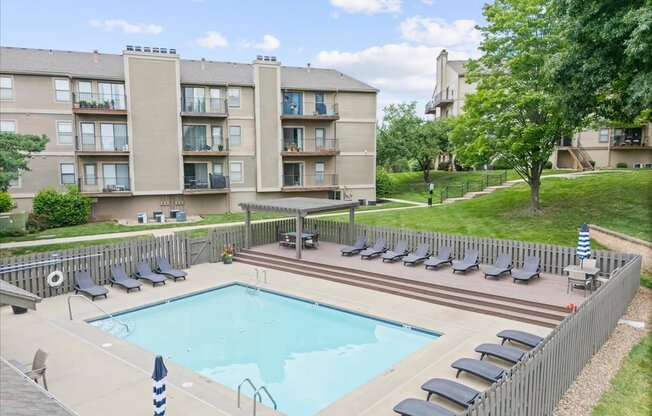 A large swimming pool surrounded by lounge chairs and apartment buildings.
