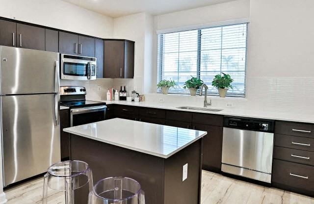 The Highland Kitchen with stainless appliances, dark cabinets, white quartz counters and light faux wood flooring