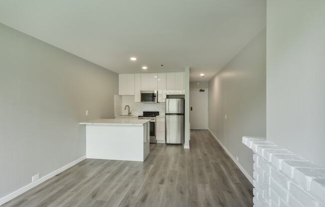 an empty living room with a kitchen with a stove and refrigerator