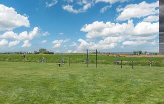 A grassy park area featuring outdoor exercise equipment on a clear day with clouds and a landscape of green fields and distant construction.