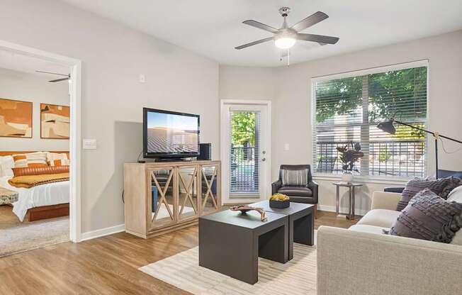 A living room with a grey couch, a wooden cabinet, a television, and a window with blinds.
