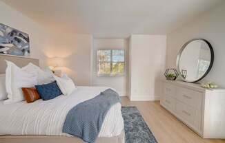 A bedroom with a large bed, a round mirror, and a window with a view of trees.