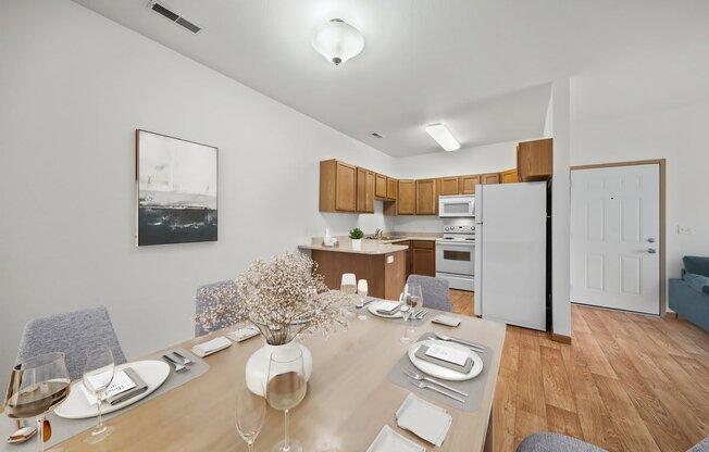 a dining area with a wooden table and chairs and a kitchen in the background
