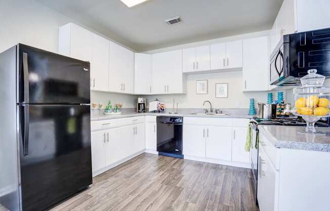 A black fridge in a white kitchen with wooden floors.
