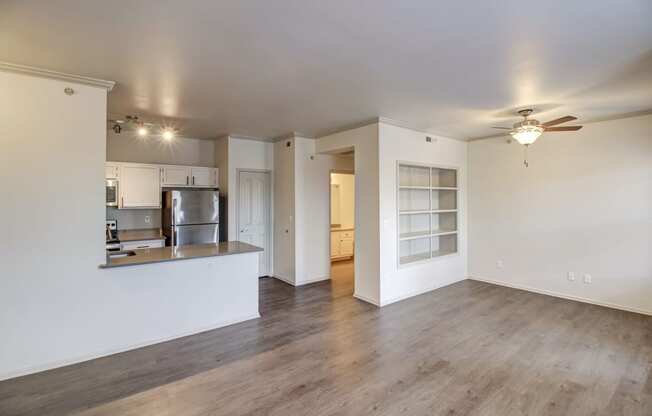 an empty living room with a kitchen in the background