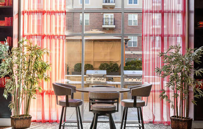 A dining room with a table and chairs in front of a window with red curtains.