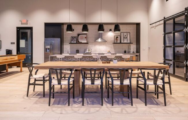 a large wooden table with chairs and a kitchen in the background