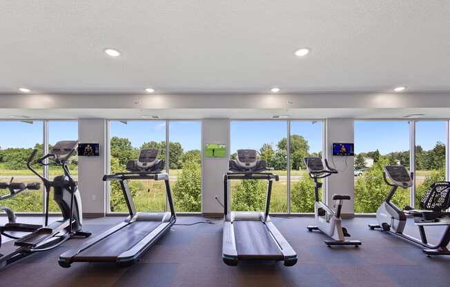 a gym with cardio equipment and windows with a view of a field