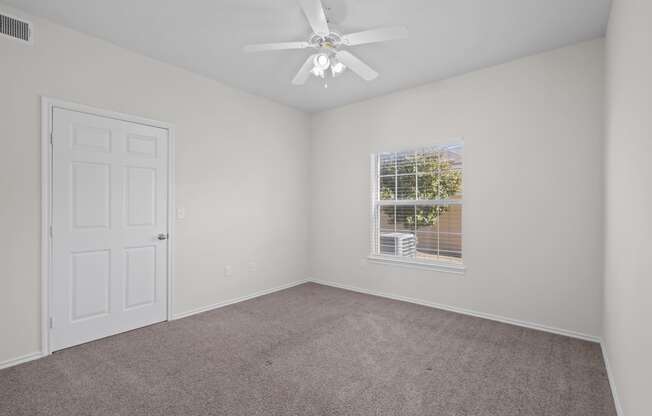 an empty bedroom with a ceiling fan and a window