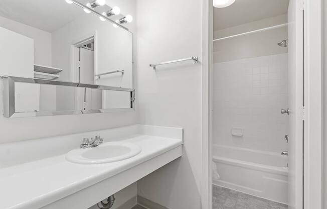 A white bathroom with a sink, mirror, and bathtub.