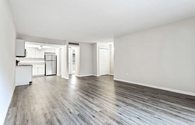 an empty living room and kitchen with white walls and wood floors