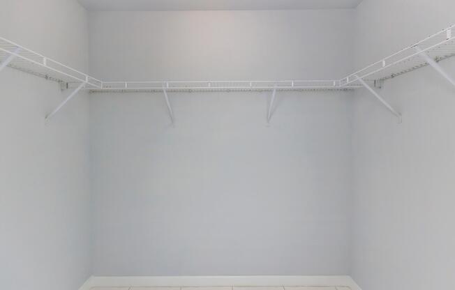 Empty closet with grey walls and white wire shelving on either side. The floor is tiled, and there are no items or clothing visible inside the closet. The overall appearance is clean and spacious.