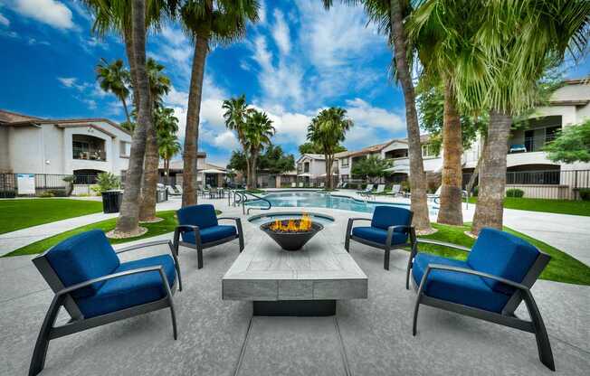 A patio with blue chairs and a fire pit surrounded by palm trees.