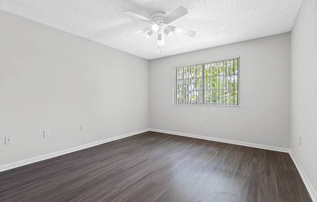A room with a ceiling fan and a window with bars.