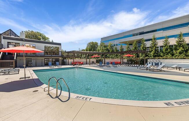 a swimming pool with chairs and umbrellas next to a building at Troy Place Apartments - Troy, MI, Troy, Michigan
