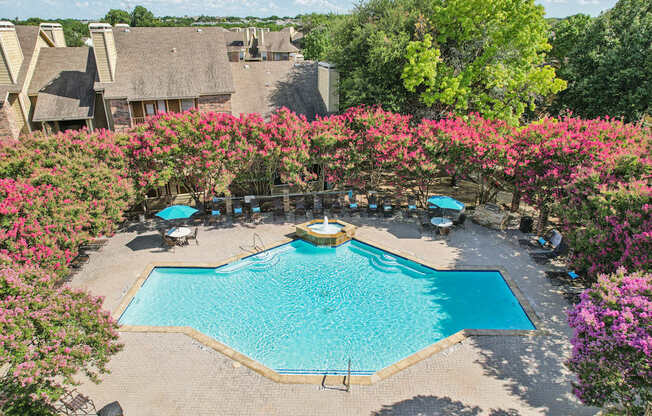 A pool surrounded by pink flowers and a thatched roof building in the background.
