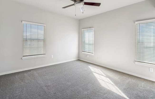 an empty living room with a ceiling fan and two windows