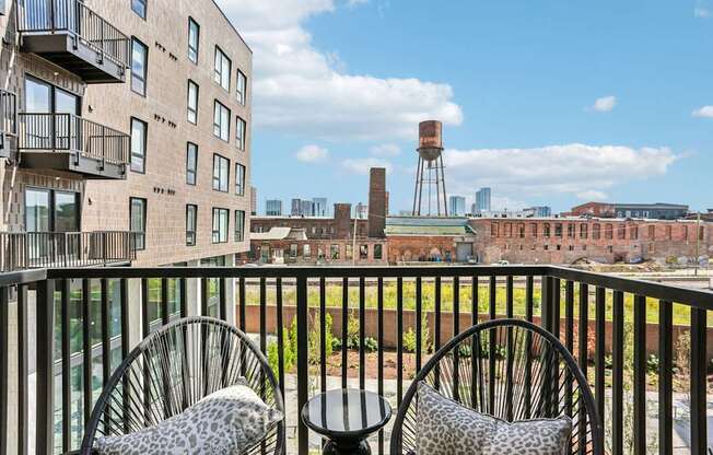 Two chairs with leopard print cushions are on a balcony overlooking a cityscape.