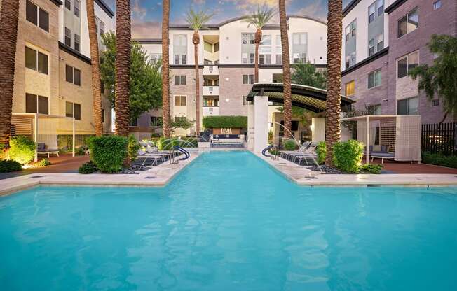 A swimming pool surrounded by palm trees and lounge chairs in a residential area.