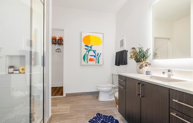 A bathroom with a toilet, sink, and a painting on the wall.