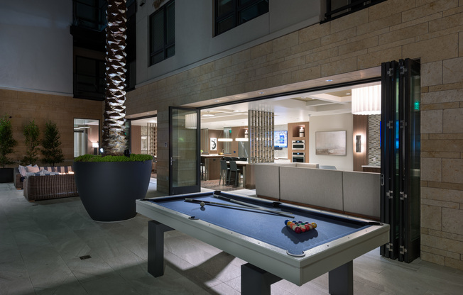 Outdoor billiards table next to the firepit and adjacent to the indoor clubhouse with full-length windows that slide away to create an indoor-outdoor space.