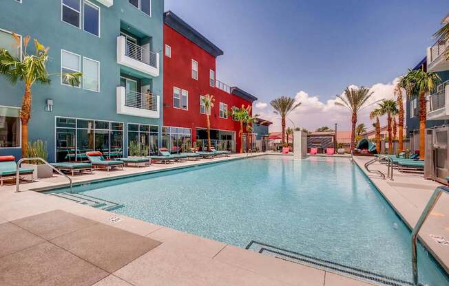 A swimming pool in front of a red building with palm trees.