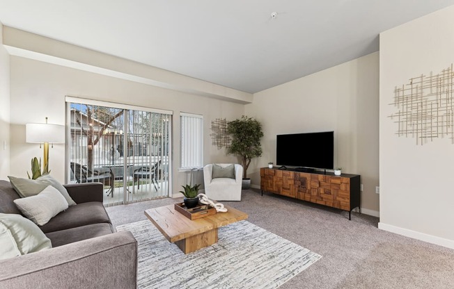 A living room with a grey couch, a wooden coffee table, a flat screen TV and a large window.