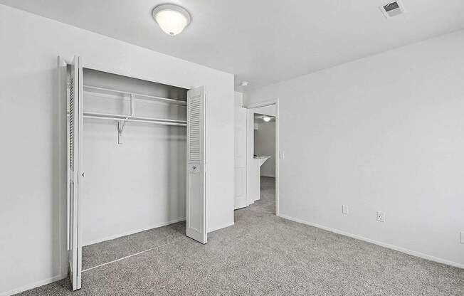 A white bedroom with a large closet and carpet at Trappers Cove Apartments, Lansing