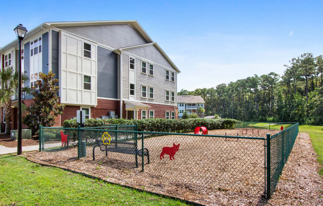 a fenced in dog park in front of a apartment building
