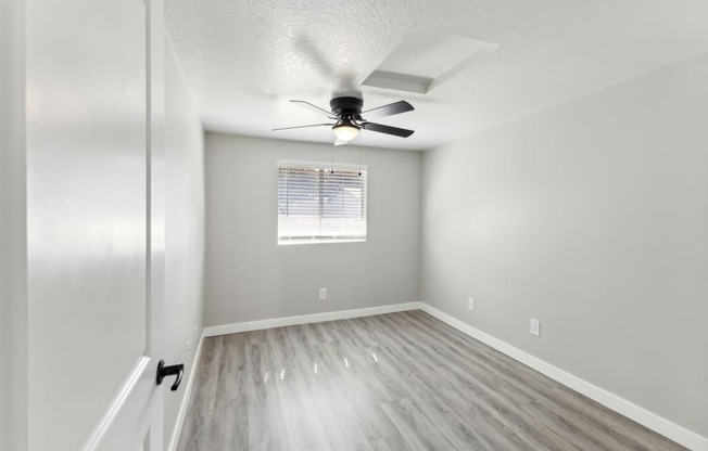 an empty bedroom with a ceiling fan and a window