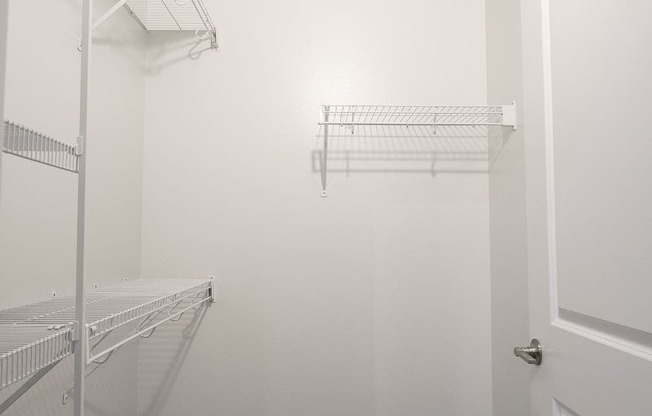 a walk in closet in a white room with shelves and a door