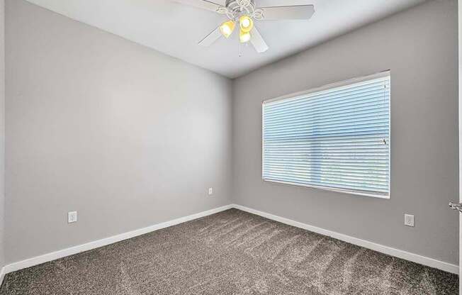 an empty bedroom with a ceiling fan and a window