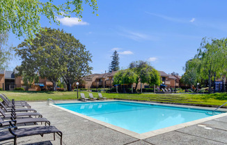 a swimming pool with chaise lounge chairs and trees in the background