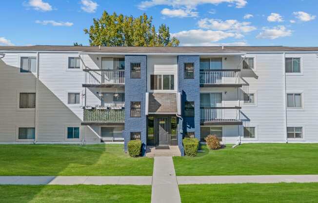 an exterior view of an apartment building with green grass and a sidewalk