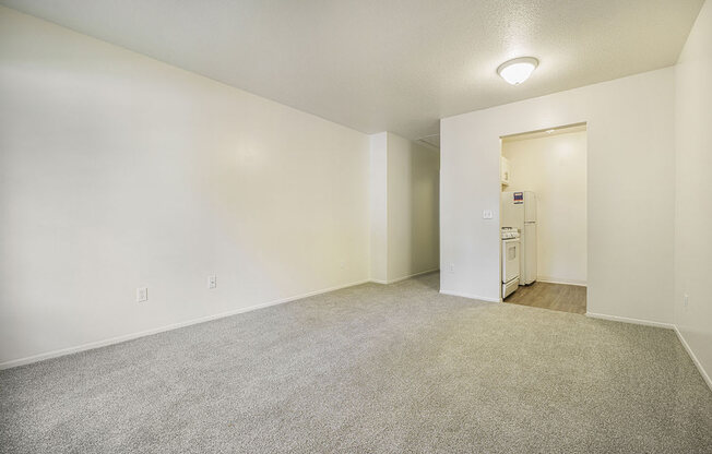 a spacious living room with carpeting and a kitchen in the distance at Newport Village Apartments, Portage, MI