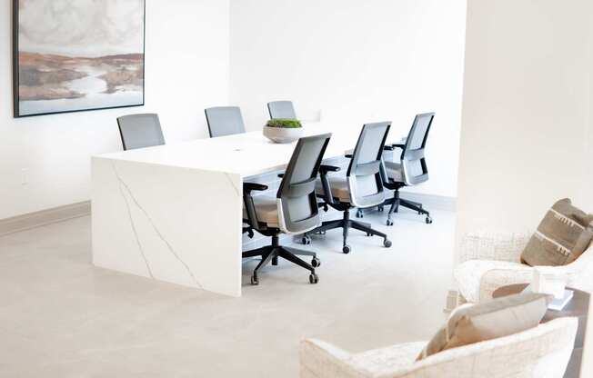 A white conference table with chairs and a painting on the wall.