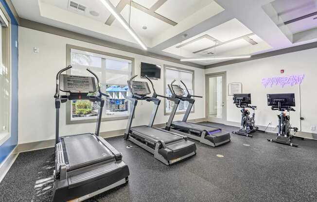 A gym with treadmills, exercise bikes, and a neon sign that says "SWEAT".