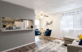 A living room with a grey couch and a dining table with blue chairs.