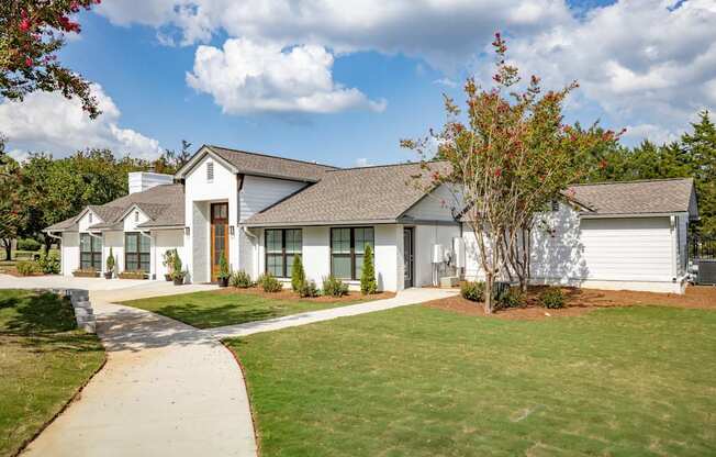 A white house with a brown roof and a tree in front.