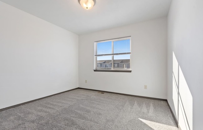 A room with a carpeted floor and a window overlooking a building.