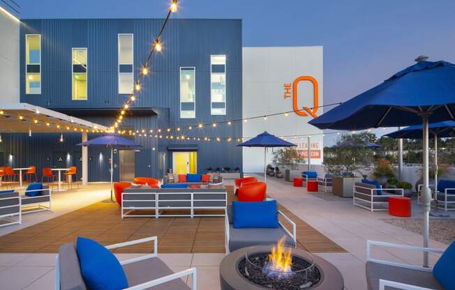 Apartments in Woodland Hills for Rent - The Q Variel Apartments - Patio with String Lights, Plush Outdoor Seating, Umbrellas, Potted Plants, and a Fire Pit