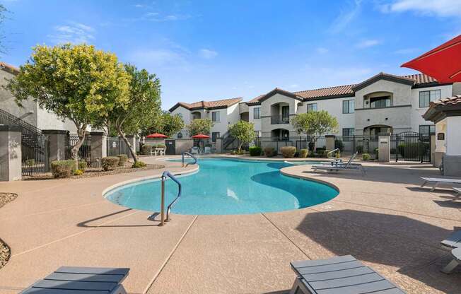 A swimming pool surrounded by a concrete patio and lounge chairs.